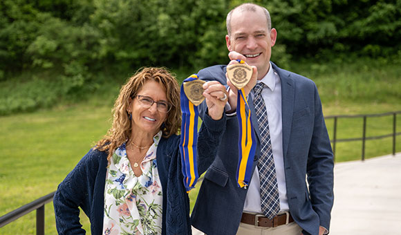 Shelly Thompson and Travis Smith hold up their Chancellor's Award medallions outside French Hall.