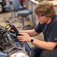 An automotive technology student runs diagnostics on a car.