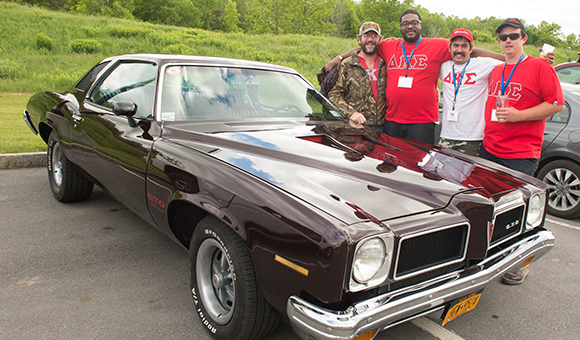 Alumni from Delta Kappa Sigma pose behind a classic car.