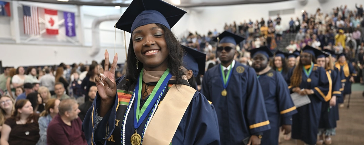 A graduate gives the peace sign as she walks with the procession to Commencement 2025.