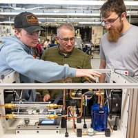 Instructor Jay Simmons works with two students on a heat pump.