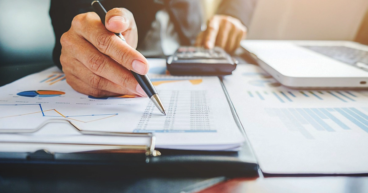 Close-up of a person reviewing a spreadsheet with a pen and calculator.