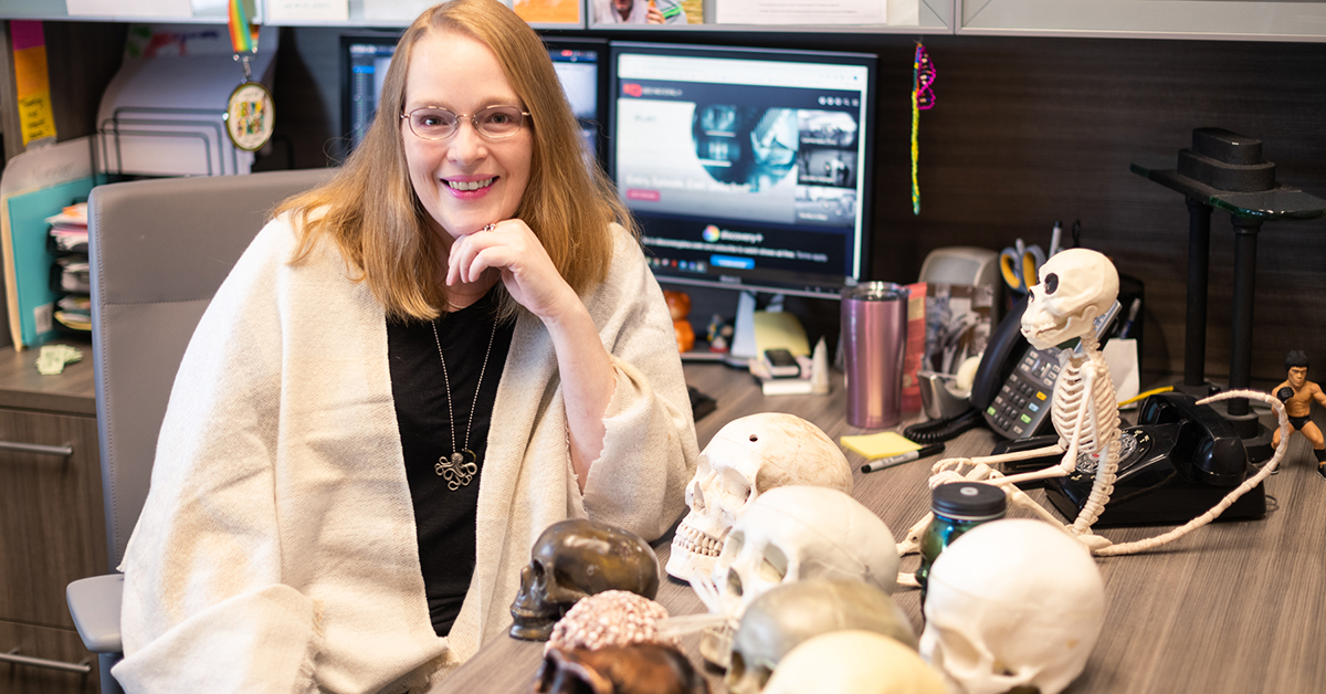 Kelly Ficner sits at her desk with many model skulls.