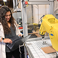 A student programs a yellow mechanical arm.