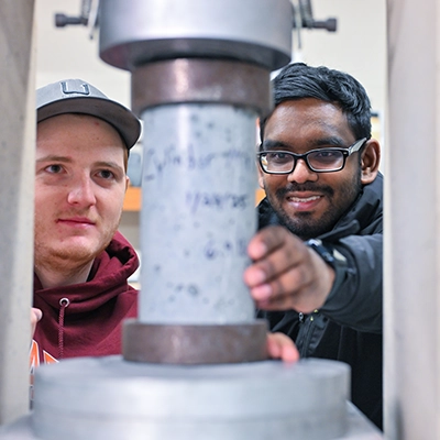 Two students test the stability of a concrete cylinder.