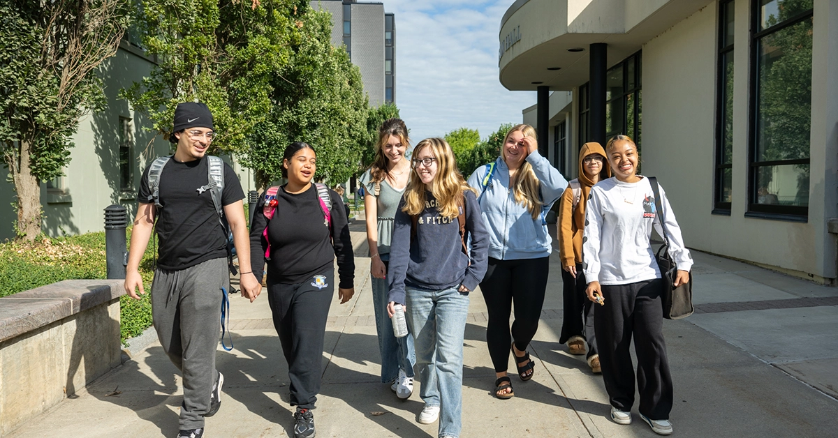 A group of seven TRiO students walk through the plaza outside Cook Hall.