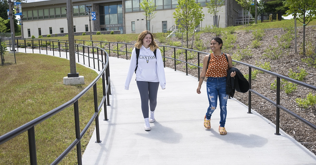 Two students walk down the sidewalk from French Hall.